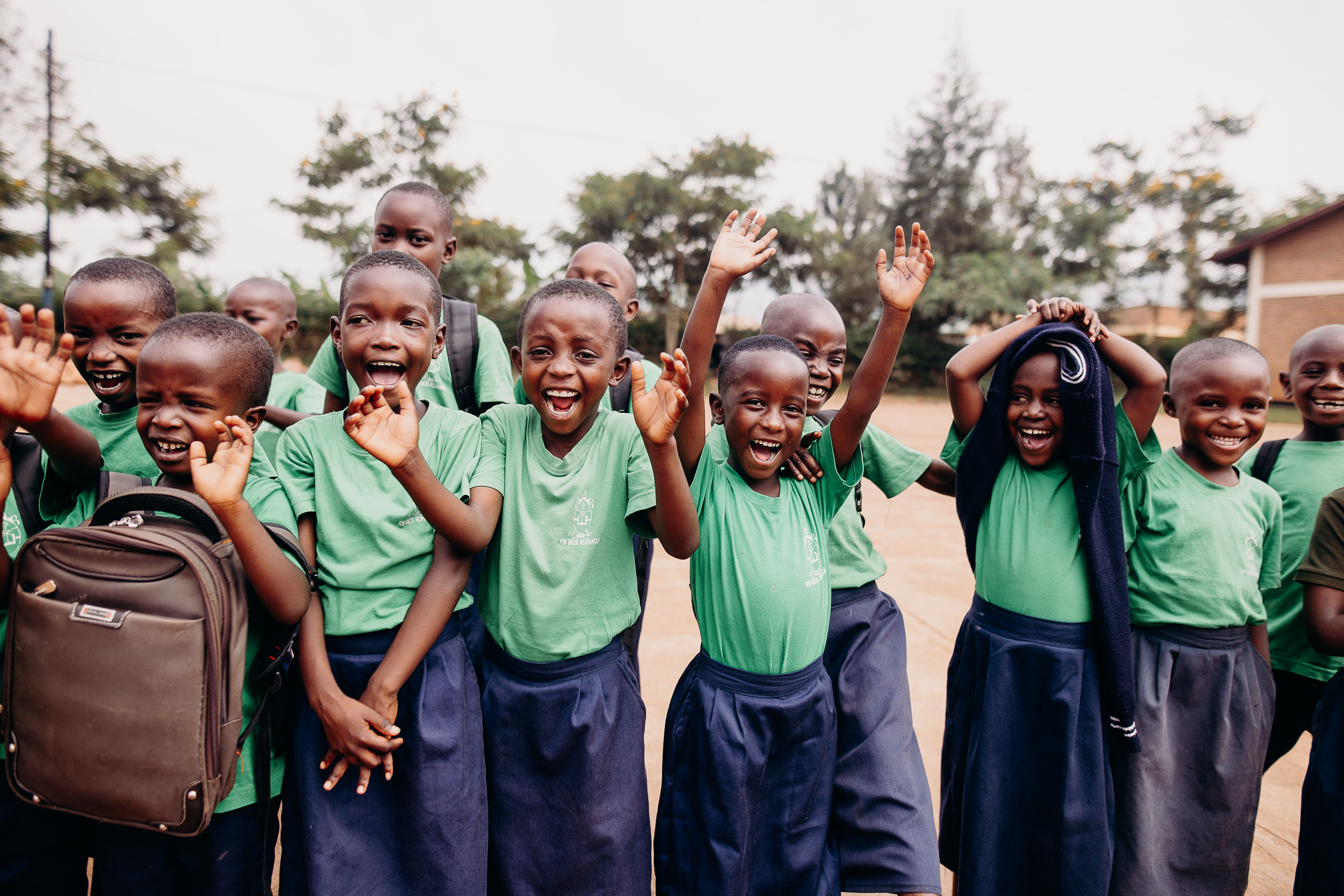 A group of children wearing green and navy school uniforms laugh and clap in front of the camera