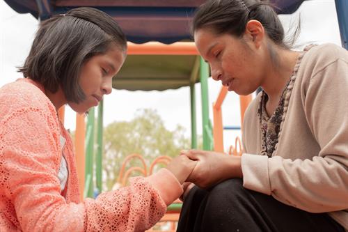 adult woman holds hands with young girl in prayer