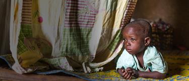 Child laying near fabric curtain and looking out