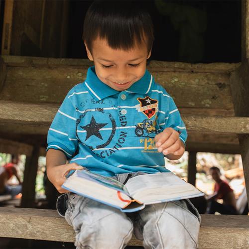 A boy sits and looks at the Bible in his lap.