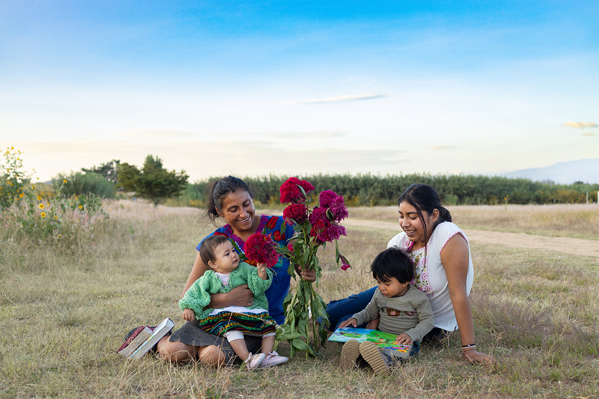 Mothers sit with their children on the grass and hold flowers.