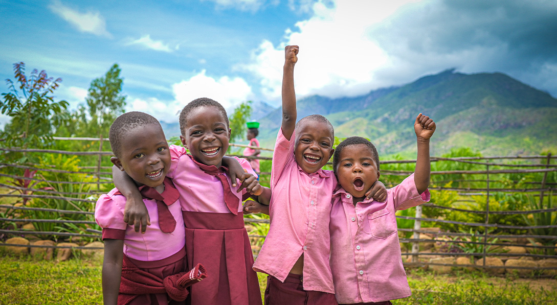 Children in pink shirts stand in front of a mountain and smiile