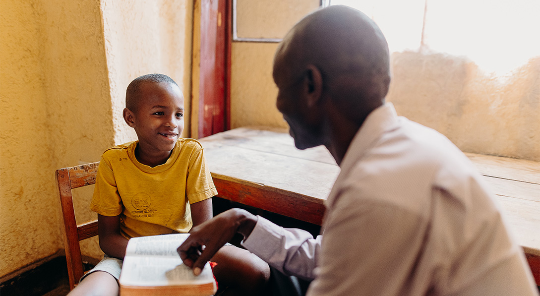 A dad looks at his smiling son while he holds a Bible.