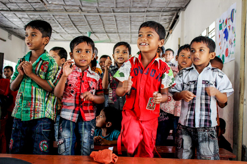 A group of children stand up and smile as they participate in the classroom