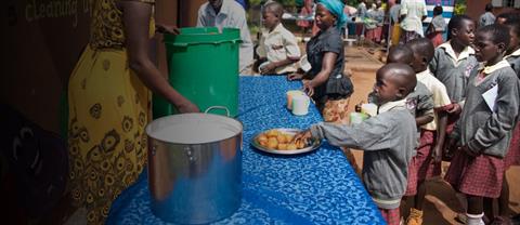 Children standing in a line to recieve food from a woman at a table.