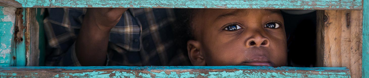 a boy peeking through the slats of a fence wall