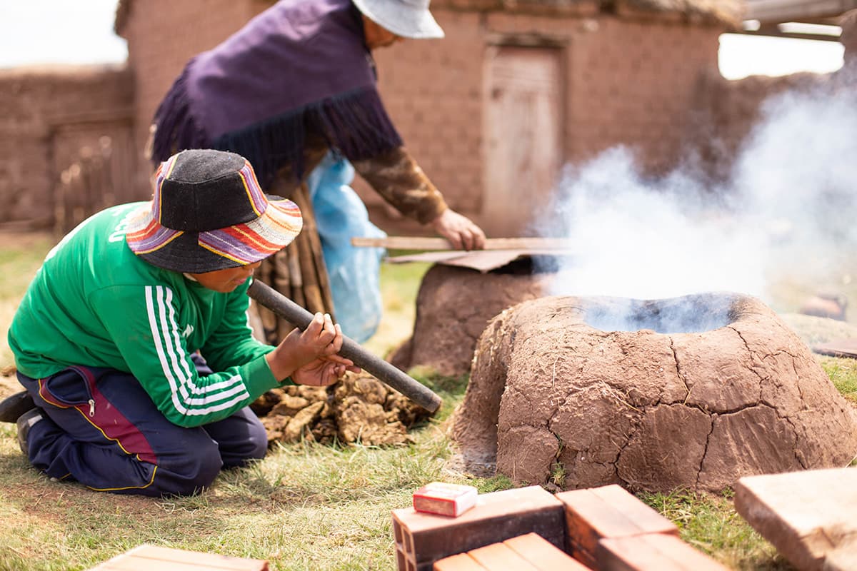 Boy outside blowing on a fire using a pipe