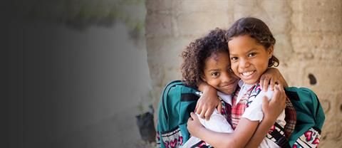 Two girls hug and smile in school unifroms