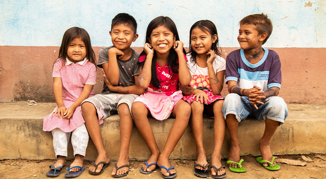 Image shows five children sitting on a concrete step and smiling for the camera.