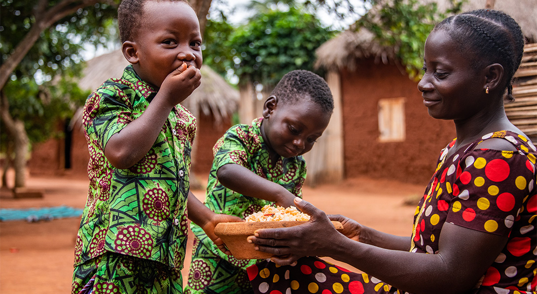 Two young boys in brightly colored outfits eat from a bowl.