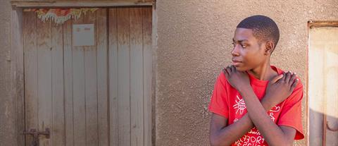 A boy in a red shirt crosses his arms across his chest while looking to his right