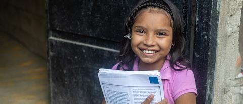 A child holds letters from her sponsor and smiles