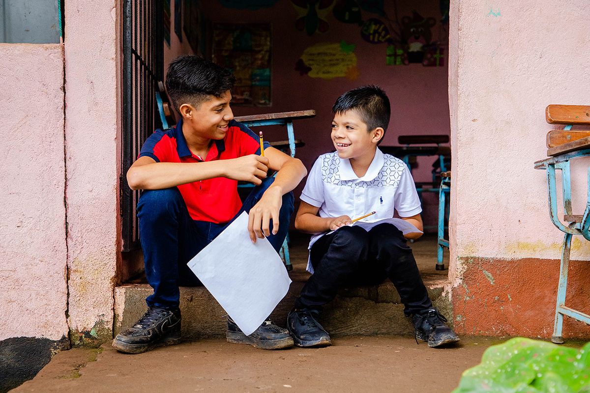 2 boys sit outside of their school