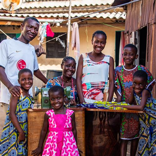 a family stands around their mother at a sewing machine