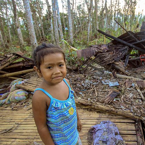 girl in blue shirt stands in front of rubble