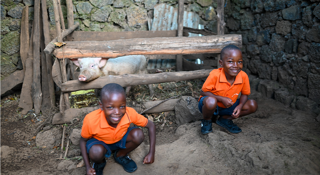 Twins stand in front of pig and smile at camera