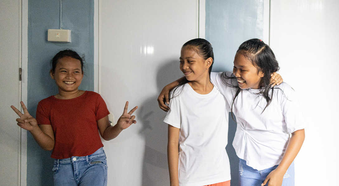 Three girls laugh and pose for a photo outside the doors of a bathroom area.