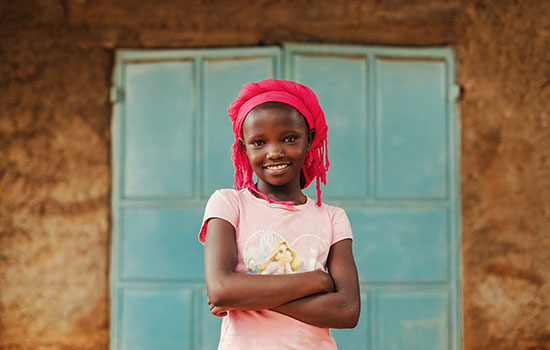 A young girl with a pink head wrap stands in front of blue doors