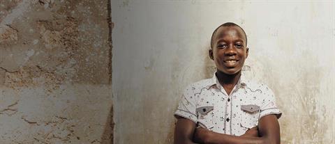 A boy crosses his arms and leans his back against a wall