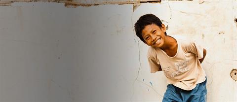 A boy in a white shirt bends at the waist in front of a white wall