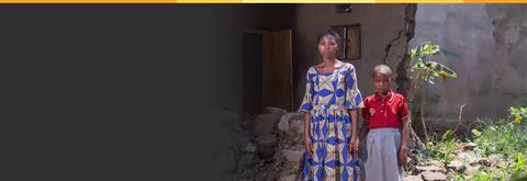 mother and child stand in front of rubble