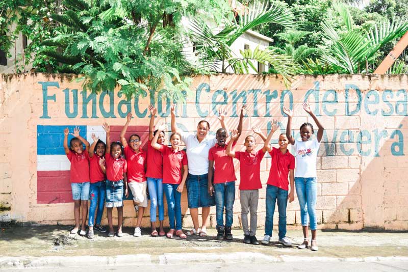 A group of children smile and wave outside of their child development center