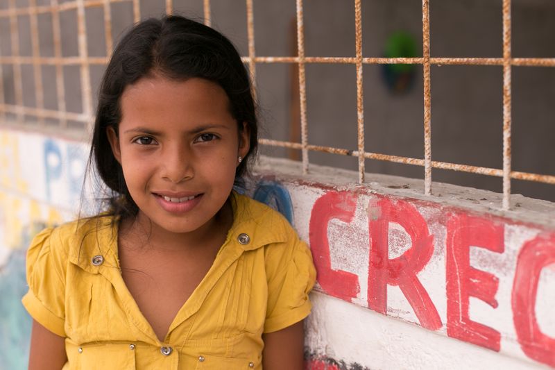 A girl stands and smiles outside her child development center