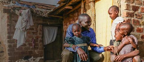 A man kneels down on one knee to speak to some poor children