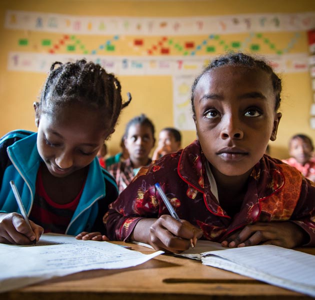 Two girls sitting next to each other taking notes in school