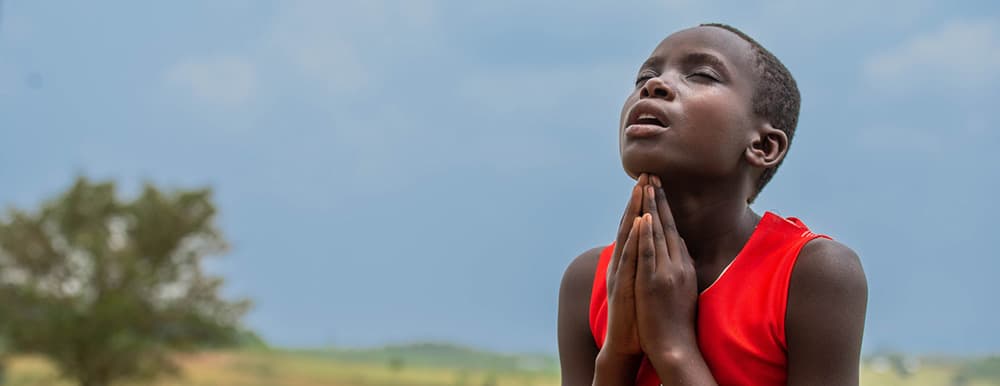 Boy praying outside with his hands together looking up at the sky.