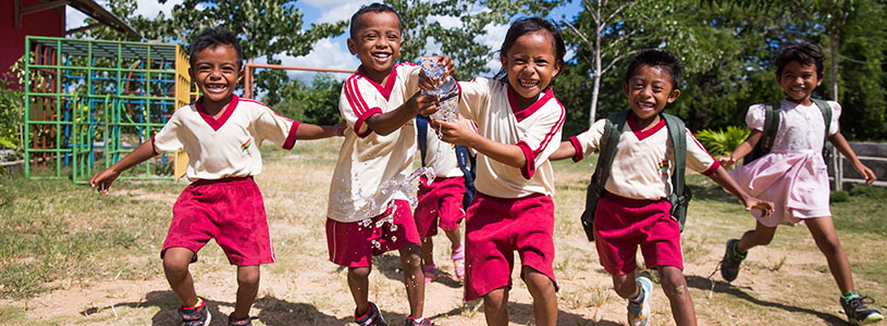 A group of running boys squeeze water out of a water bottle