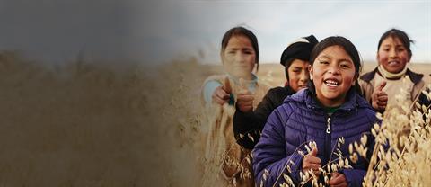 Young girls in a field smiling and giving thumbs up