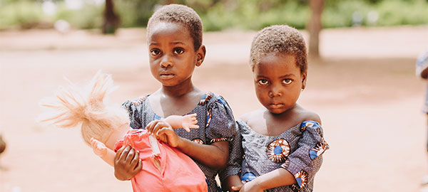 Two girls in a dry landscape stand holding a doll