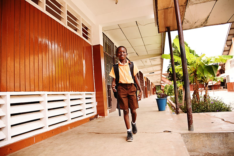 A boy smiles wlaking through school with a backpack on