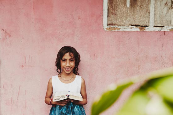 A girl holding a bible standing in front of a pink wall