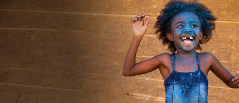 A young girl laughs with blue paint on her face