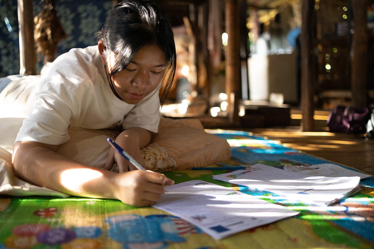 Girl writing a letter on the floor of a room.