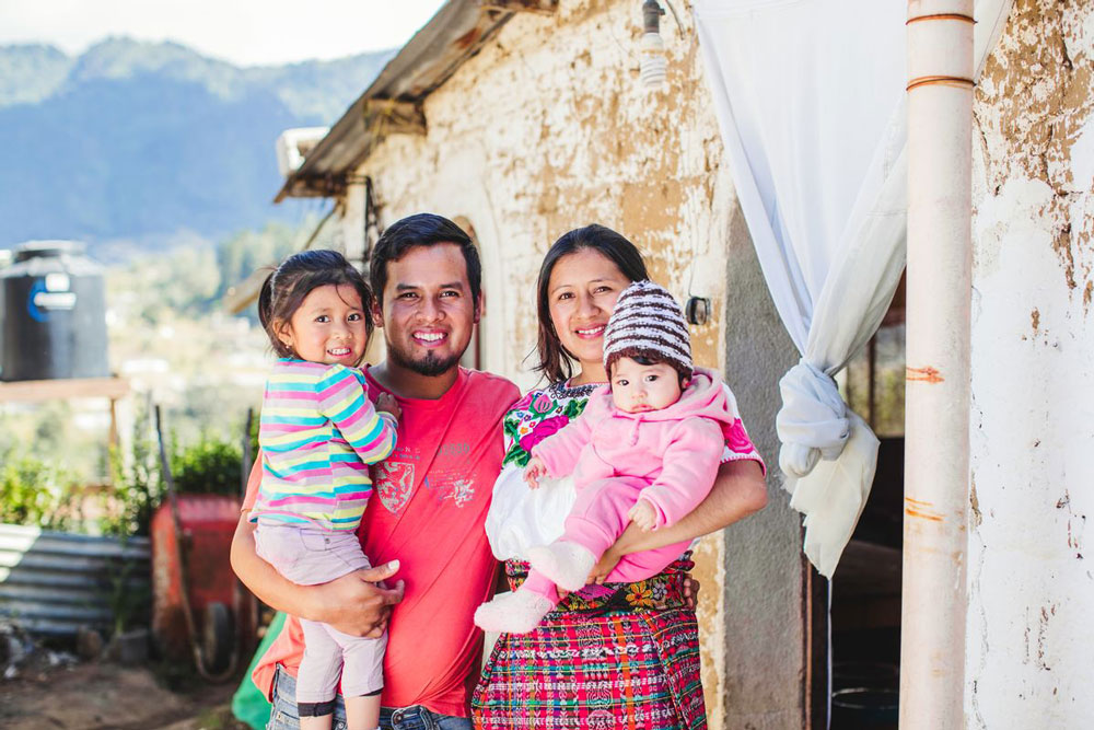 A young family stands outside of their home