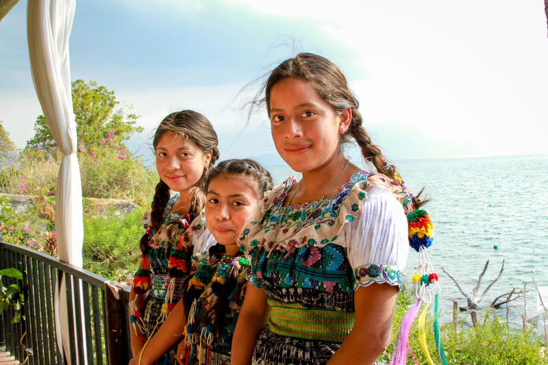 A group of three girls smile with the ocean behind them