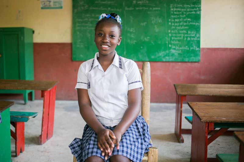 A teenage girl sits happily in her classroom