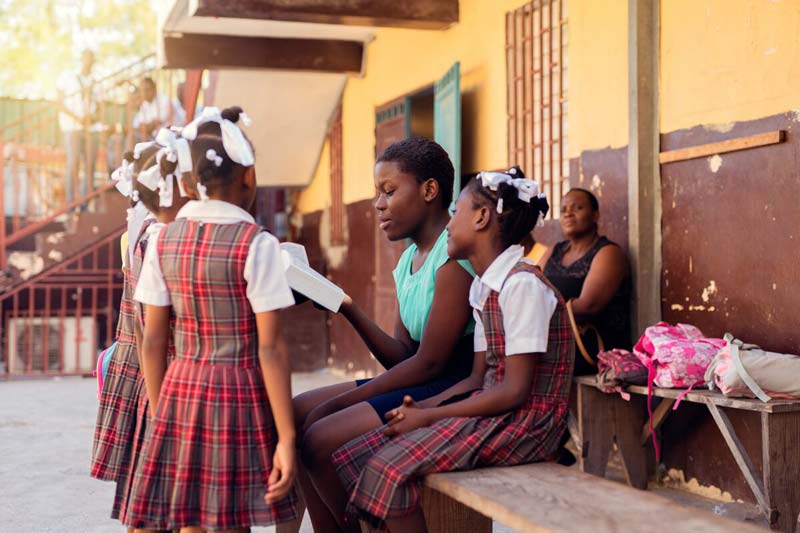 A teenage girl reads the Bible to younger girls