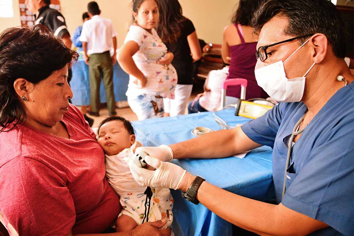 A medical professional providing a health exam to an infant in the mother's arms