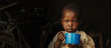 A young boy with a solemn facial expression holds a blue cup