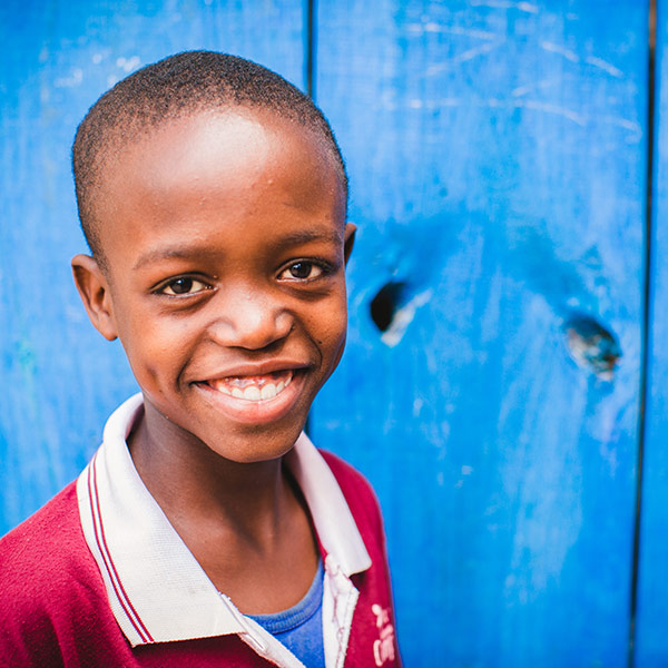 A smiling boy wearing a polo shirt stands in front of a blue wall