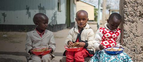 Three sitting children with plates of food in their laps