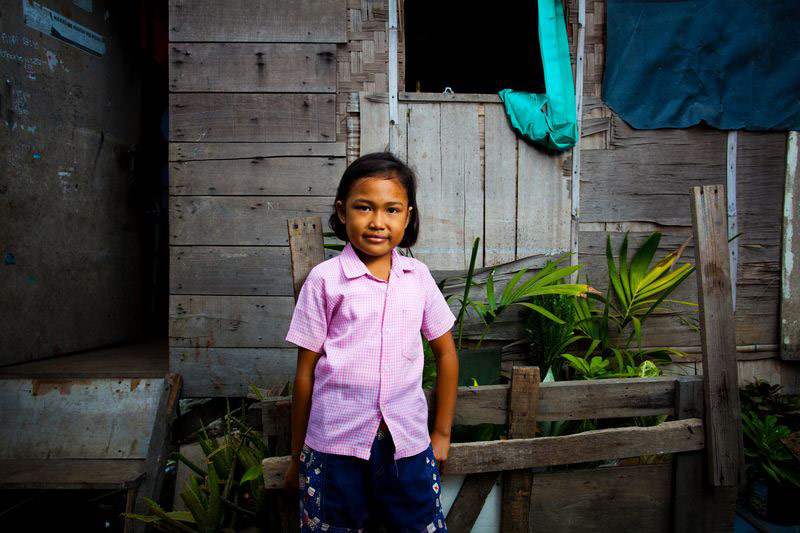 A young girl stands outside her home