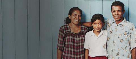 A mother, father and daughter stand in front of a blue wall with three pictures hanging on it.