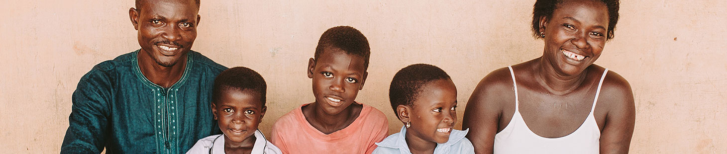 A mother, father and daughter stand in front of a blue wall with three pictures hung on it.