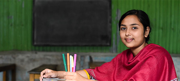 A young girl in a red shawl sits at a desk