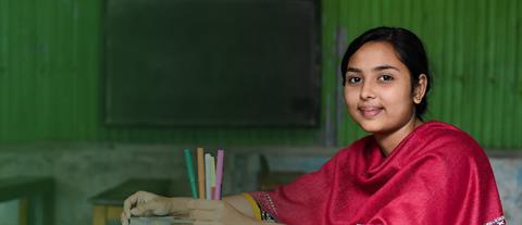 A young girl in a red shawl sits at a desk